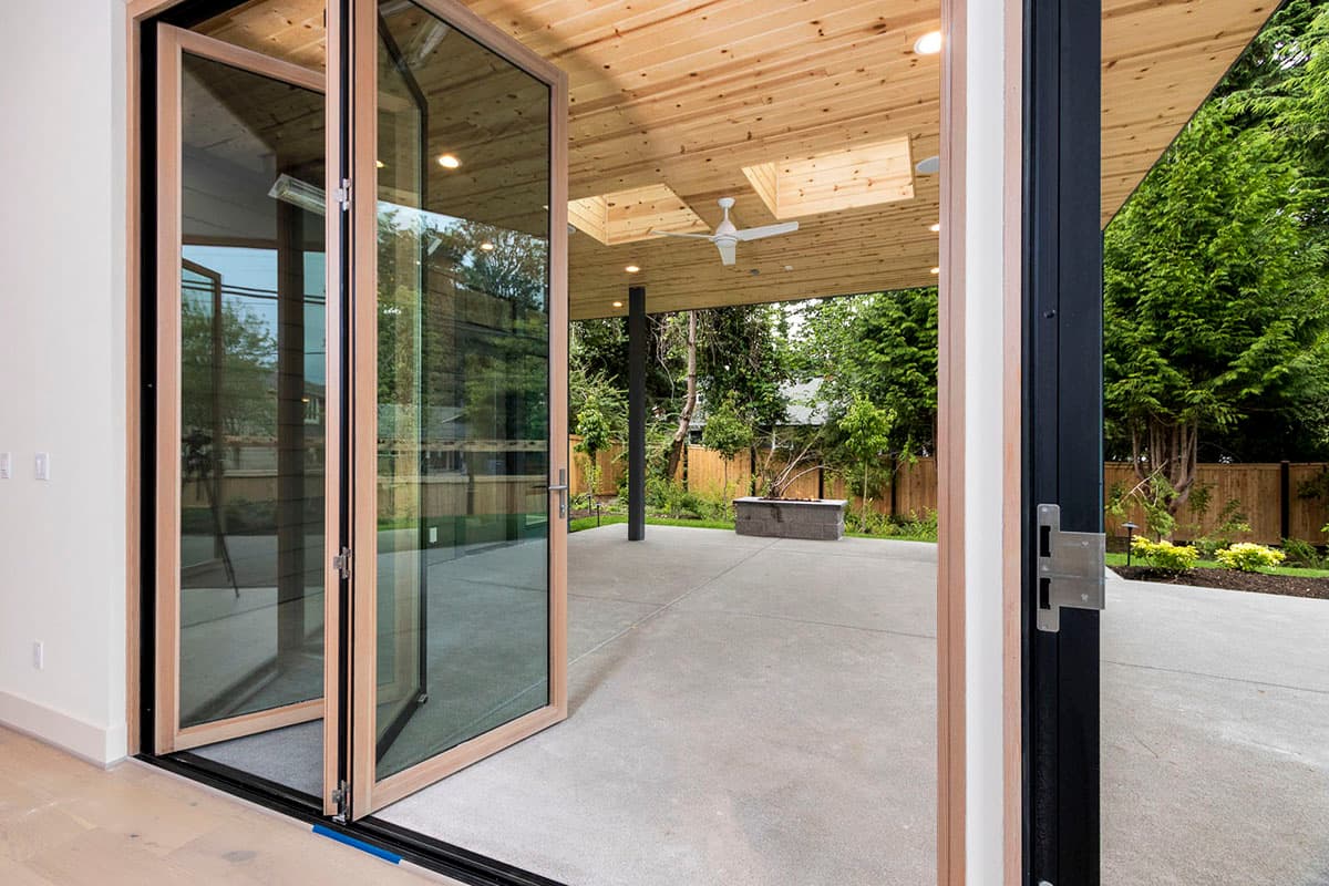 Interior view of a patio with bi-fold glass doors, exposed wood ceiling with skylights, and a fire pit visible.