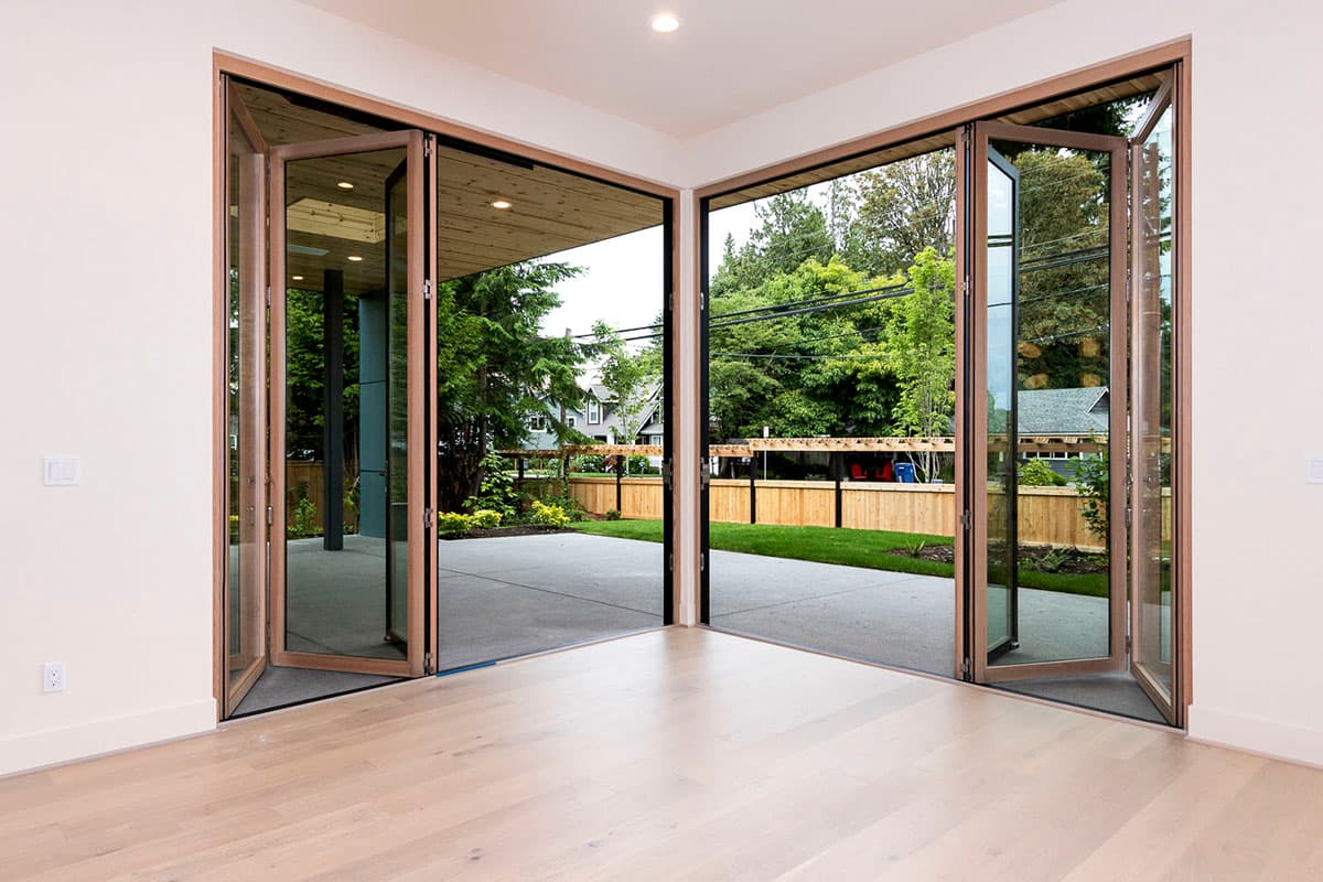 Interior view of a room with corner bi-fold glass doors opening to a patio and backyard.