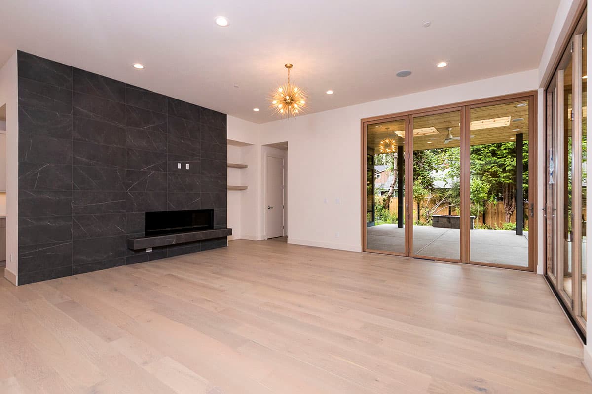 Interior view of a living room with a dark tiled fireplace, light wood floors, and folding glass doors opening to an outdoor patio.