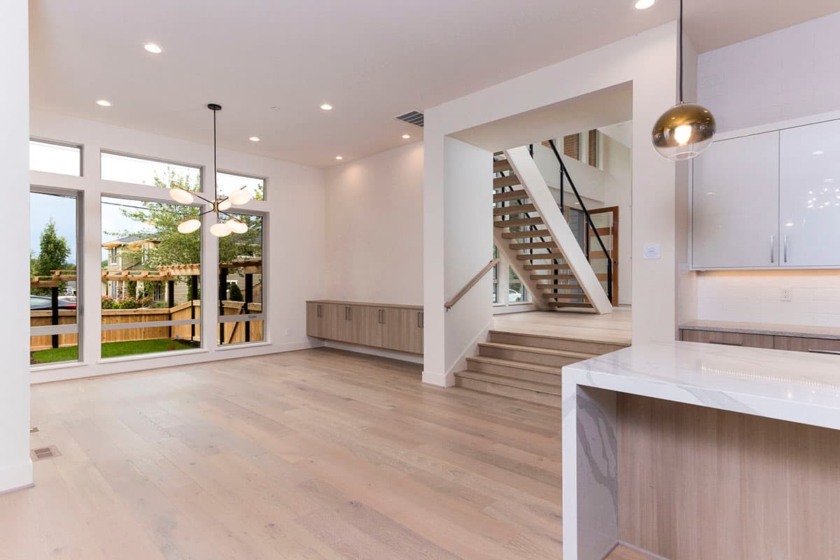 Interior view of modern home with open layout, large windows, floating staircase, and kitchen island.