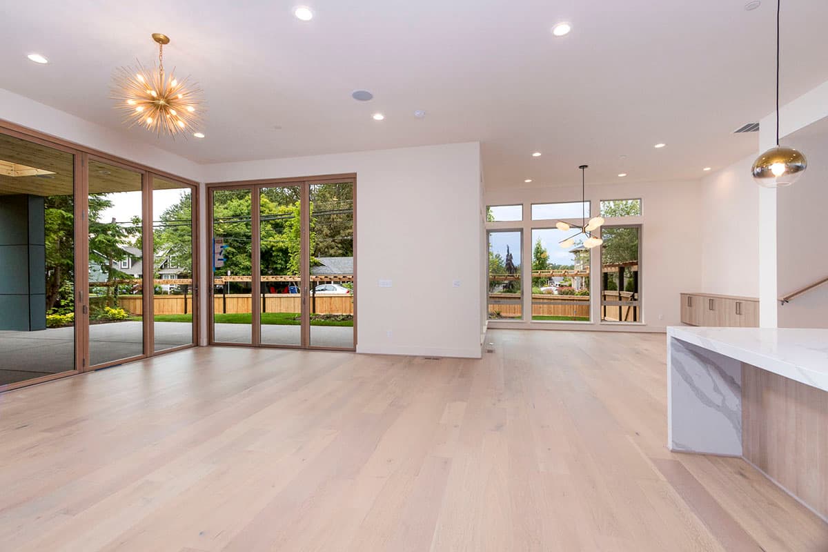 Interior view of a modern house with an open-concept living area, large folding glass doors, and contemporary lighting fixtures.