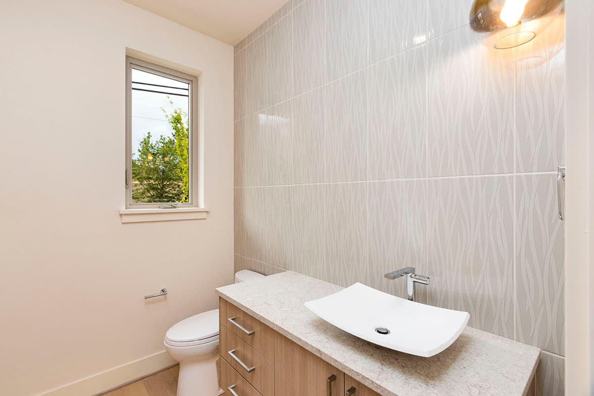 Powder room with toilet, wood vanity, vessel sink, and patterned tile wall.