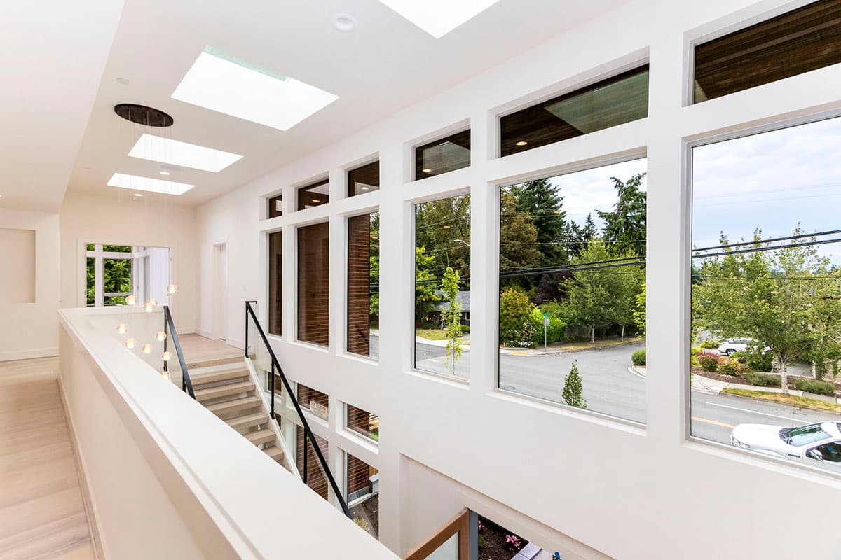 Interior hallway with skylights, open staircase with glass railing, and large banks of windows overlooking the street.