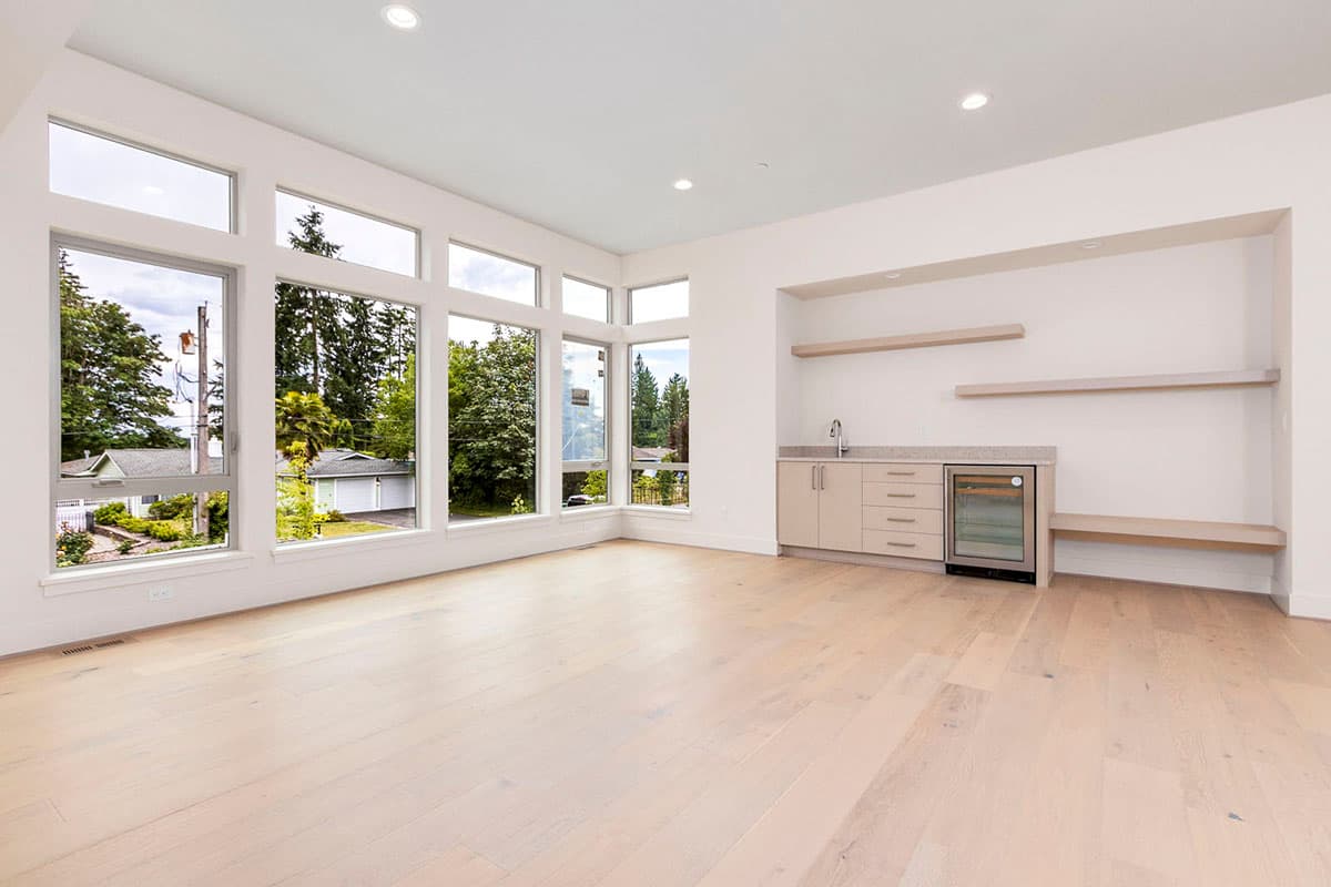Interior view of a room with large corner windows, wet bar, and light wood flooring.