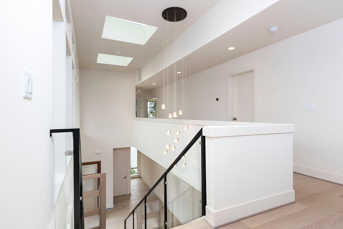 Modern interior hall with skylights, glass railing staircase, and multi-tiered chandelier.