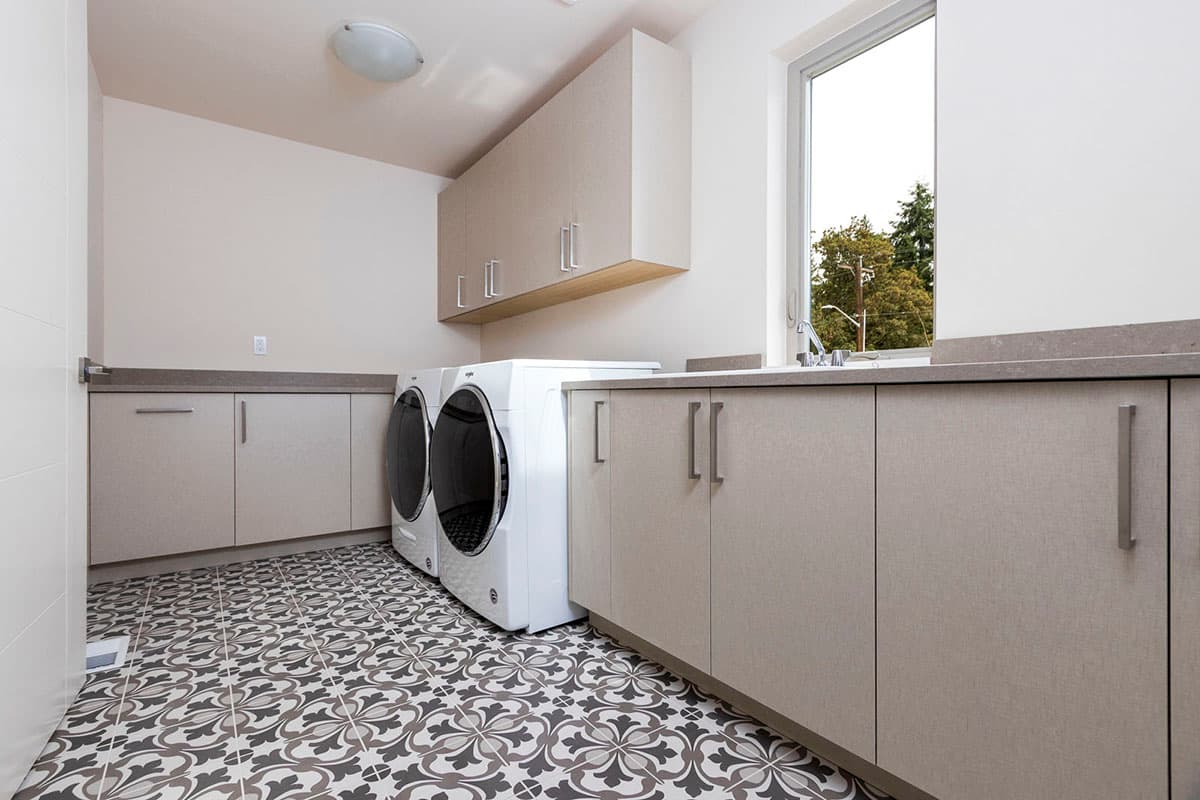 Laundry room with modern cabinets, stacked washer and dryer, countertop sink, and decorative tile floor.