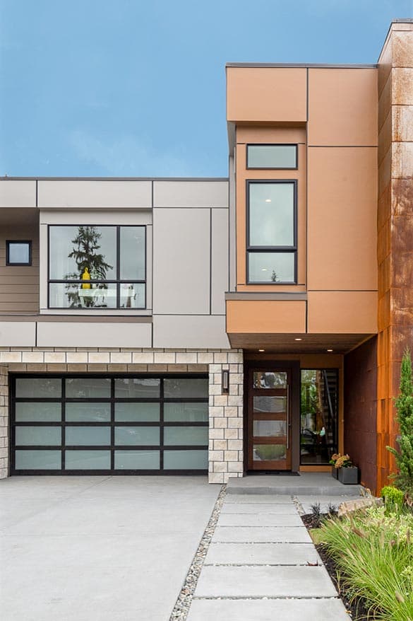 Modern house exterior with a garage, glass-paneled door, and multi-level facade featuring varied materials and large windows.