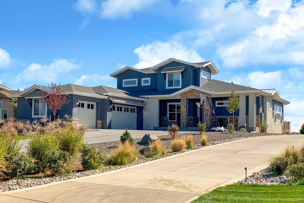 House plan exterior. Two-story home with a mix of siding styles, multiple gables, and attached garages. Features a stone facade and a long driveway.