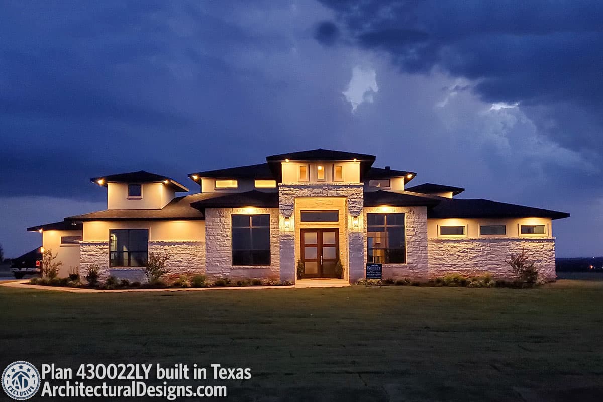 House plan exterior of a single-story modern home with stone accents, multiple gables, and a prominent entrance with glass double doors.