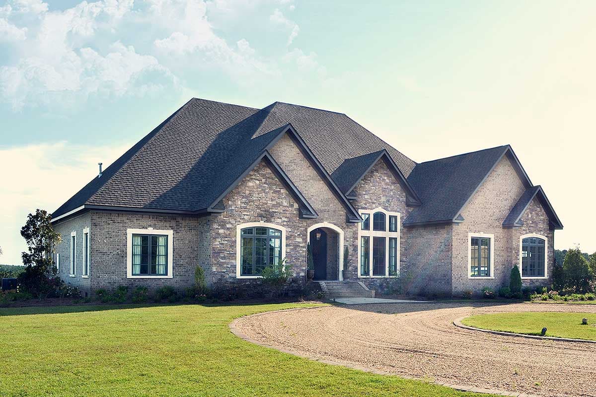 House plan exterior, single-story dwelling with stone and brick facade, arched entryway, and multiple gables.