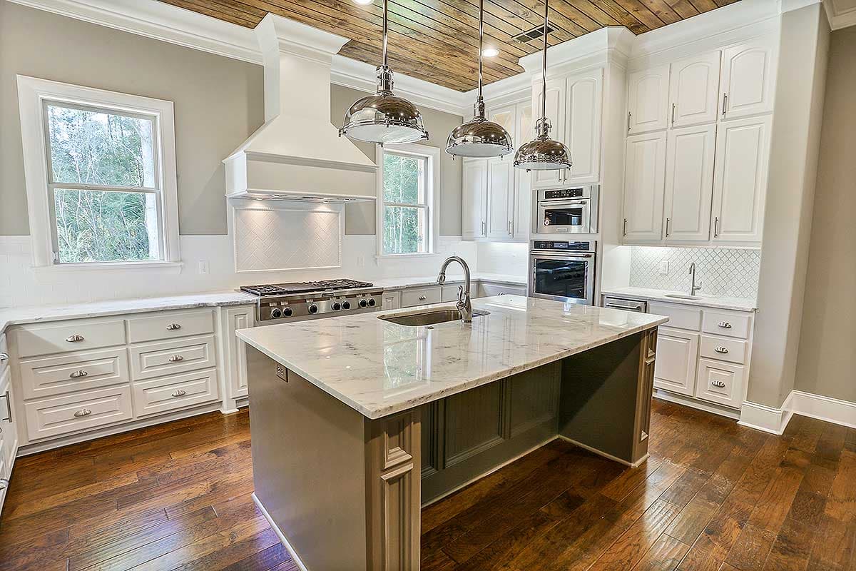 Kitchen interior with central island, professional gas range, paneled appliances, white cabinetry, marble countertops, and wood ceiling.
