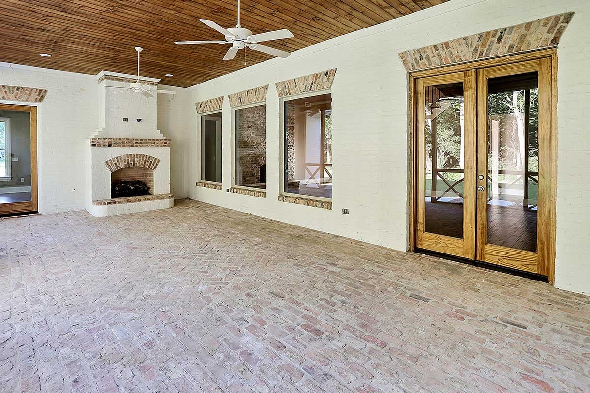 Covered porch with white brick walls, a brick fireplace, wood plank ceiling, and double glass doors.