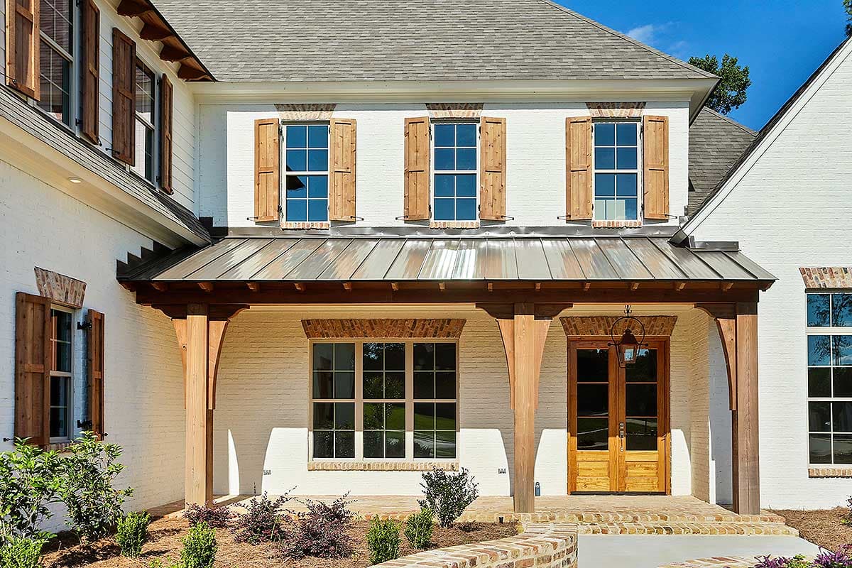House plan exterior: Two-story white brick home with metal gable roof, wood-shuttered windows, and a covered porch with wooden columns.