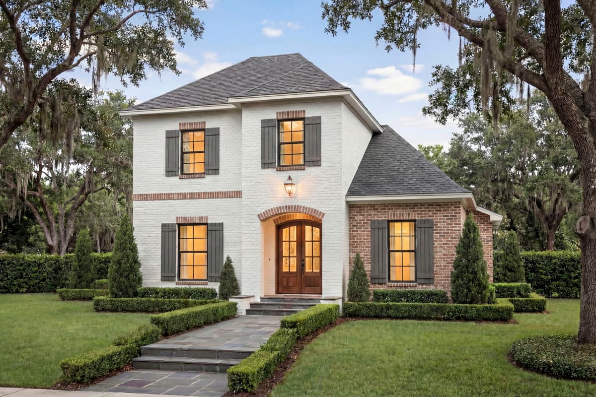 House plan exterior. Two-story brick and white painted house with dark shutters, gables, and a brick arched entry.