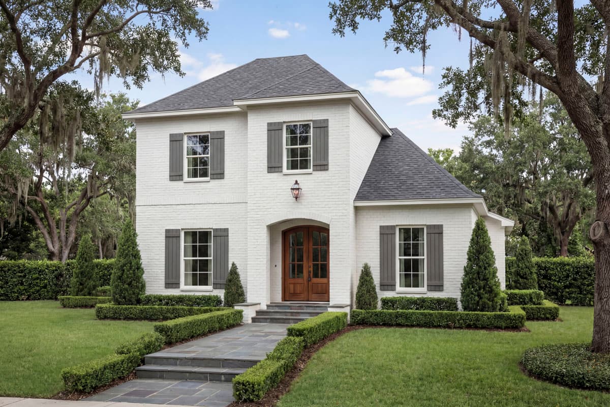 Two-story house plan exterior with white brick, gable roof, arched double front doors, and dark shutters on windows.