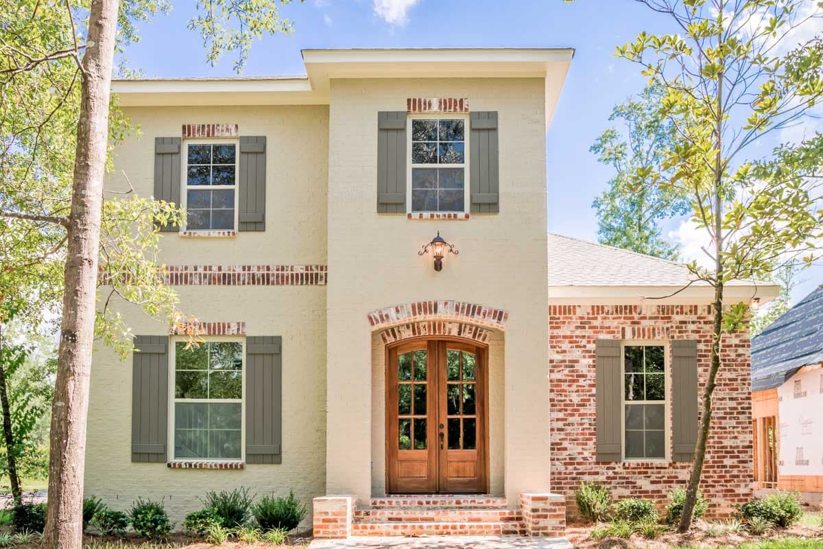 Two-story house plan exterior with brick accents, arched double-door entry, paneled shutters, and gabled rooflines.