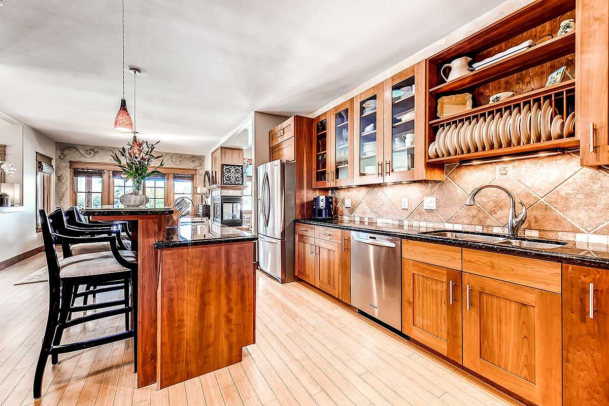 Open concept kitchen with wood cabinets, granite countertops, stainless steel appliances, island with seating, and a fireplace visible.