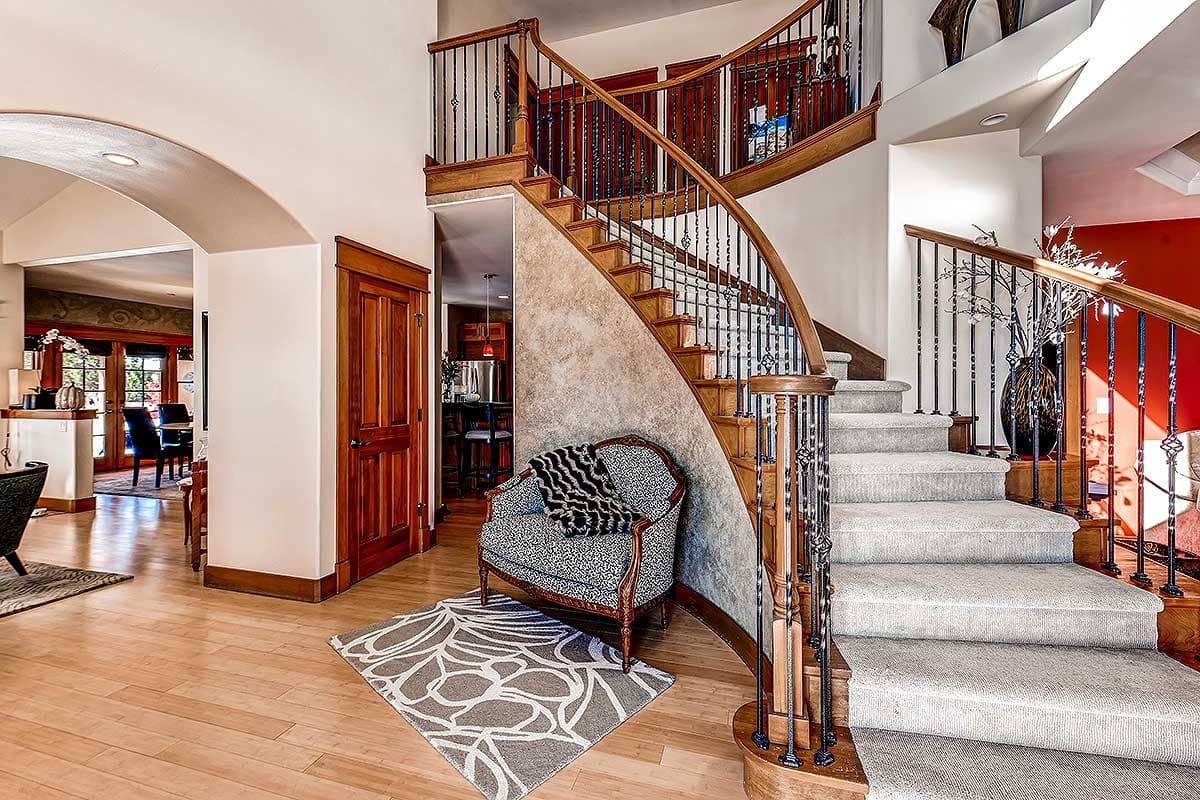 Interior view of a curved staircase with wooden banisters, ornate metal balusters, and carpeted treads.