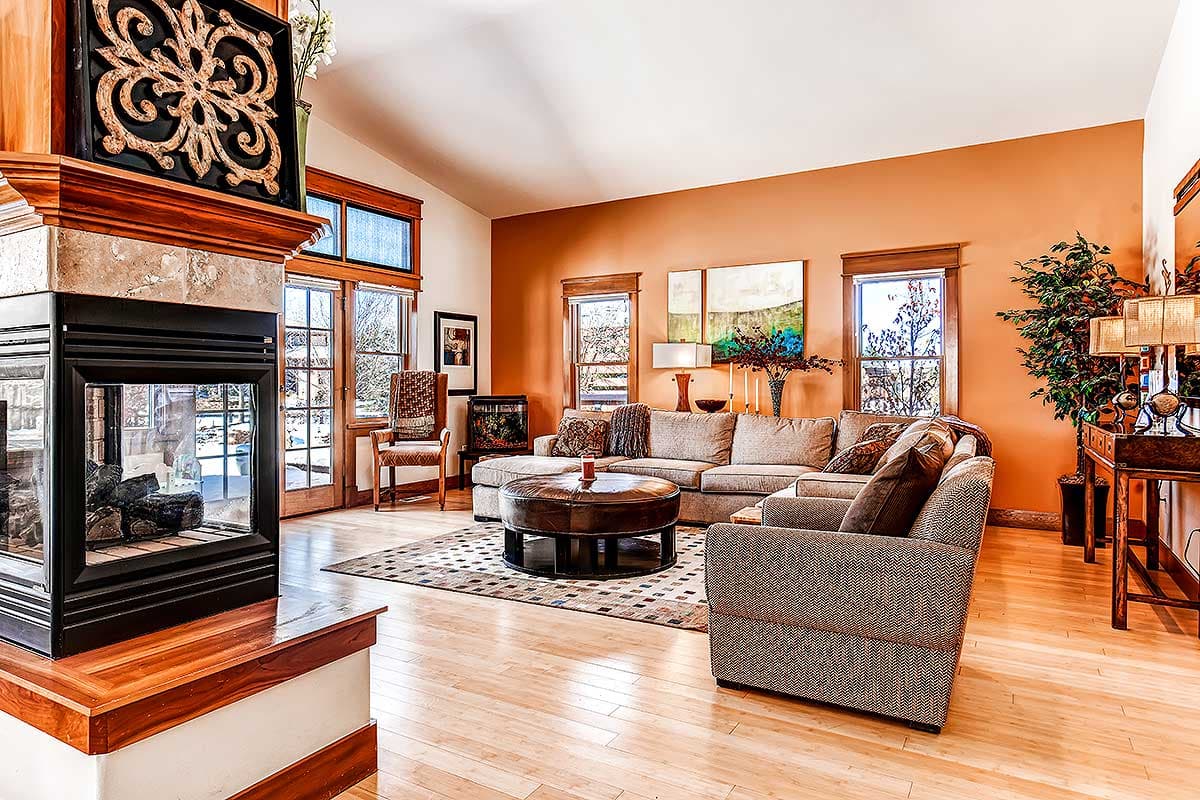 Interior view of a living room with a large corner fireplace, vaulted ceiling, sectional sofa, and leather ottoman.