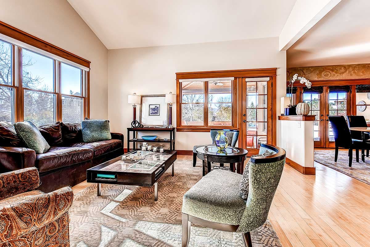 Living room with vaulted ceiling, leather sofa, glass-top coffee table, and large windows.
