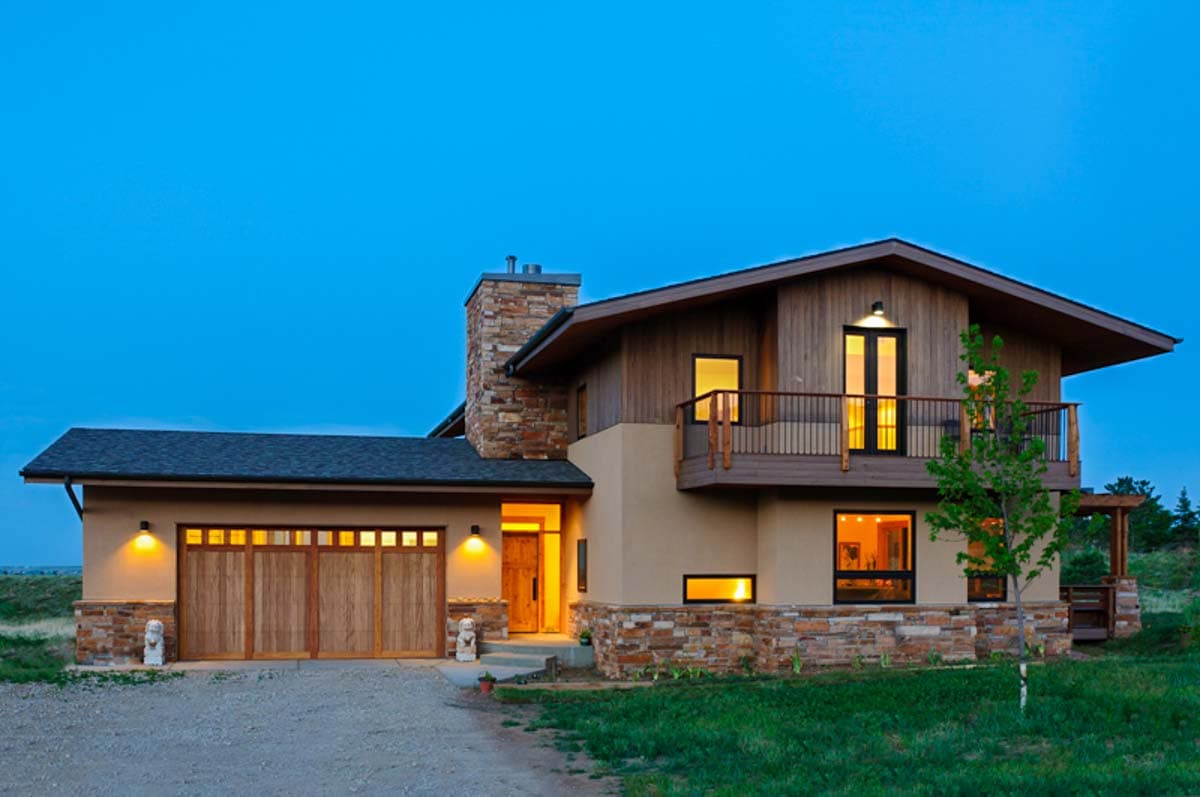 House plan exterior. Two-story home with a stone chimney, wooden garage doors, and a second-story balcony.