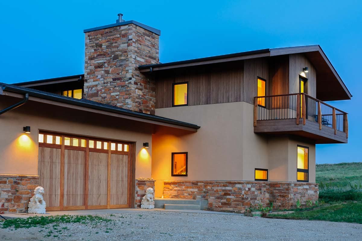 House plan exterior: Modern style with stone chimney, wood garage door, and second-story balcony.