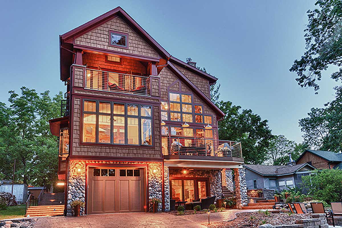 House plan exterior: Three-story home with wood shake siding, stone foundation, large windows, two balconies, and a two-car garage.