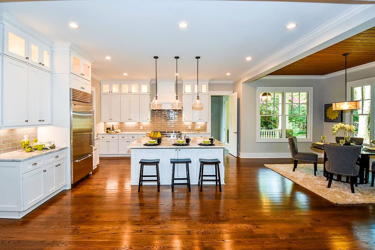 Open-concept kitchen with white cabinets, a large island with seating, stainless steel appliances, and adjacent dining area.