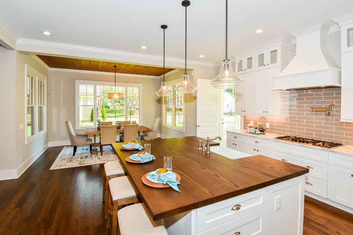 Kitchen and dining area with large island, white cabinetry, subway tile backsplash, wood floors, and dining table.