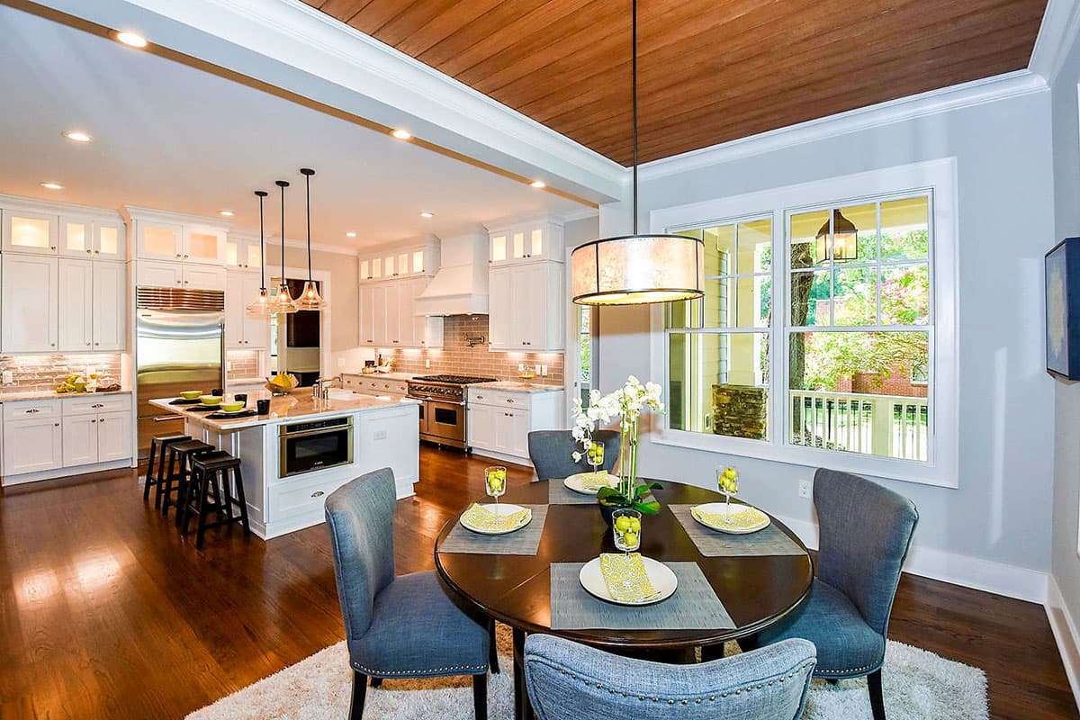 Open concept kitchen with island and dining area. Features white cabinets, stainless steel appliances, and wood ceiling.