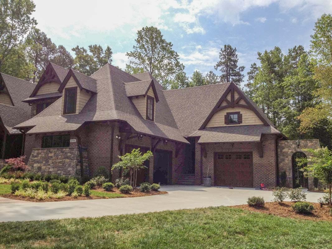 House plan exterior of a two-story home with stone and brick facade, multiple gables, dormers, and a three-car garage.