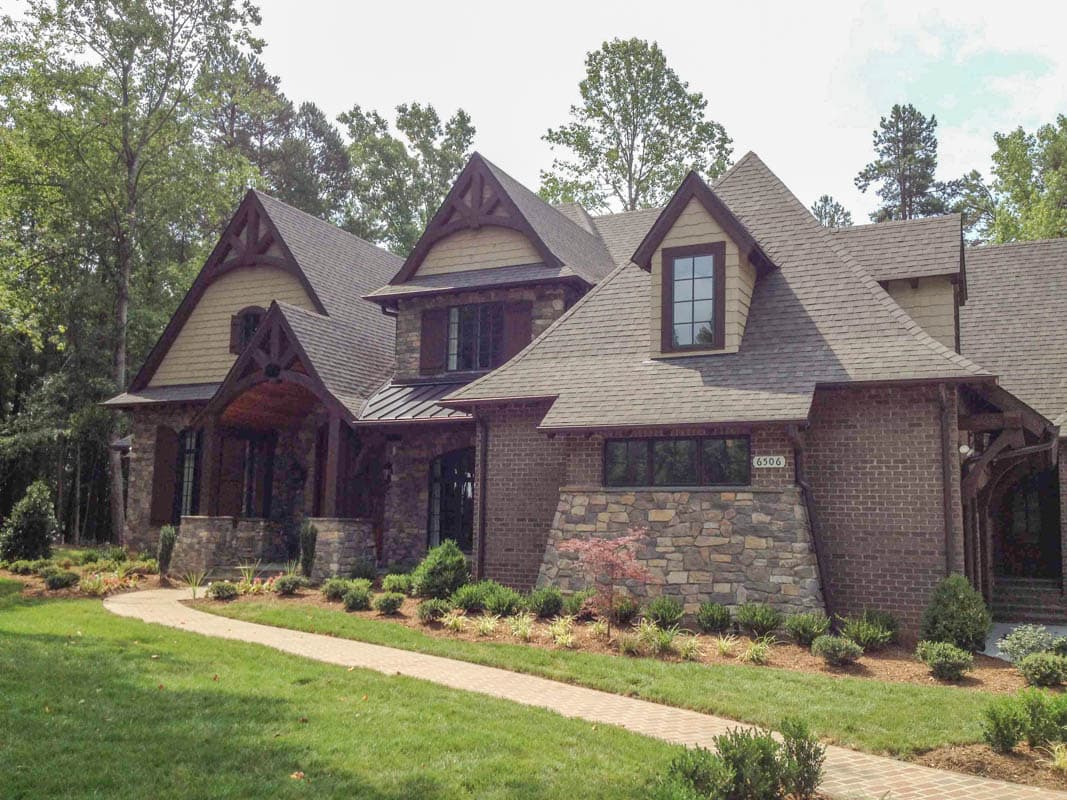 House plan exterior, traditional style with stone and brick facade, multiple gables, covered entry with timber detailing, and dormer windows.