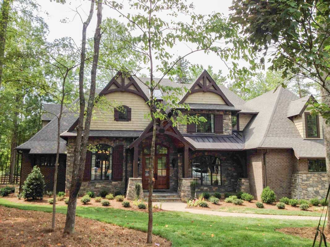 Tudor-style house plan exterior with stone and brick facade, prominent gables with decorative brackets, and covered entryway.