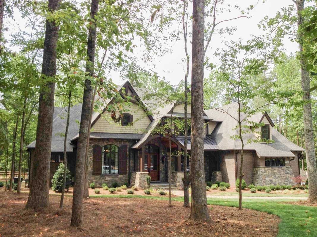 House plan exterior with stone and wood facade, prominent gables, covered entry, and dormer windows.