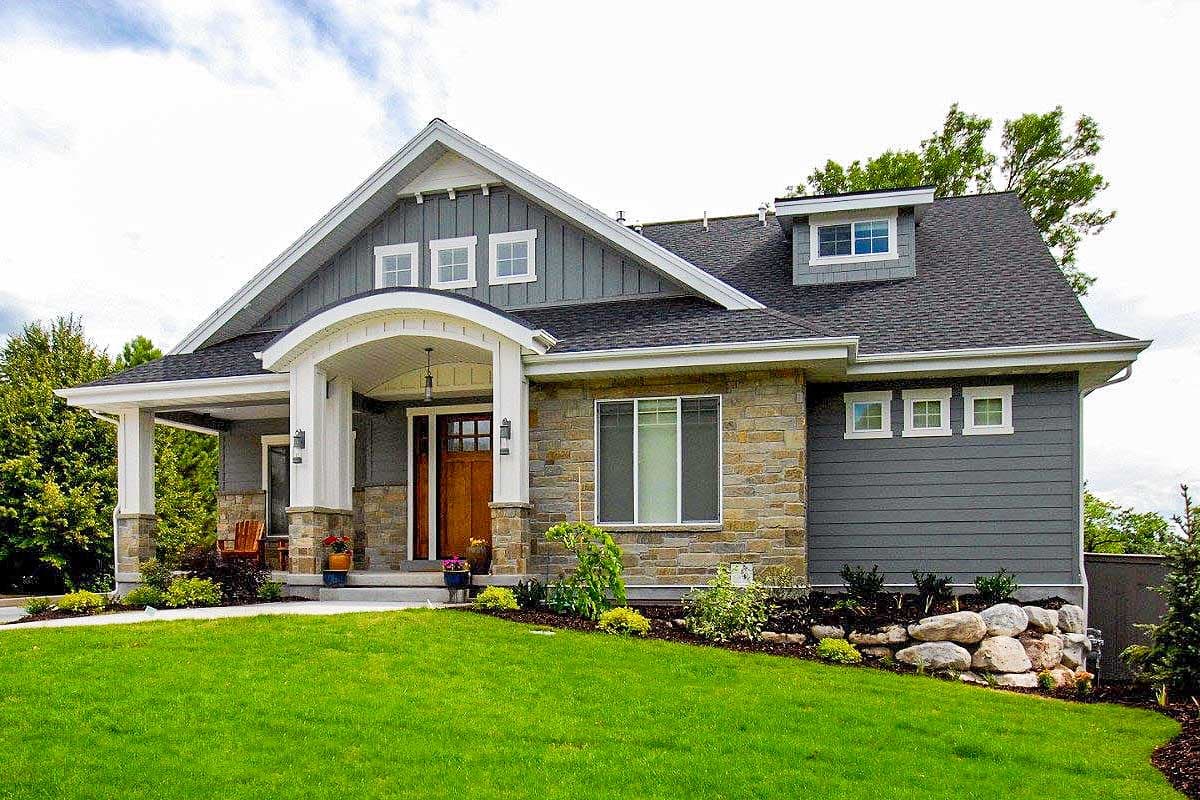 House plan exterior featuring a Craftsman style. The home has a gabled roof, an arched entry, and stone and siding facade. One story.