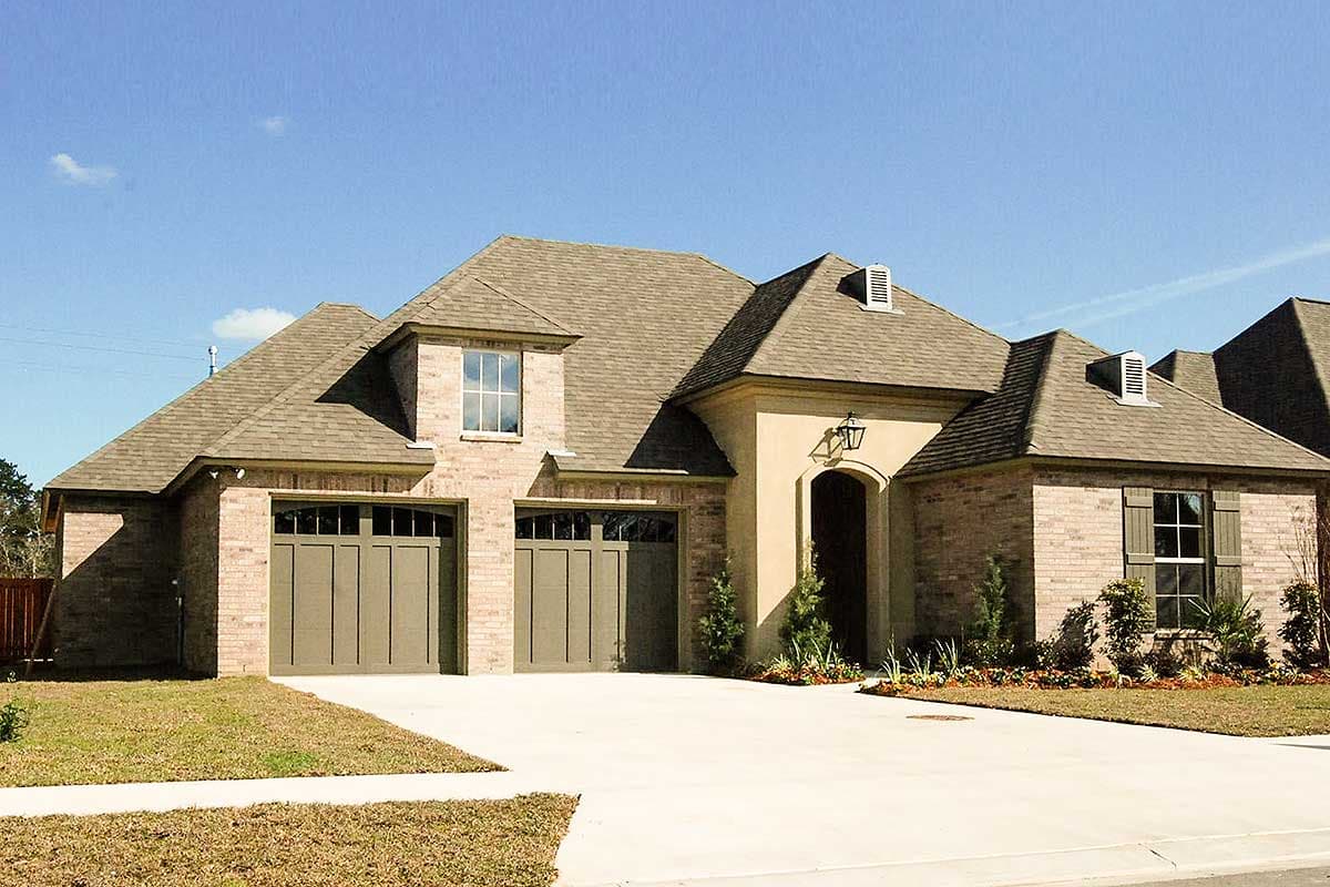 House plan exterior with brick facade, multi-gabled roof, two-car garage, and dormer windows. Features an arched entry and shutters.