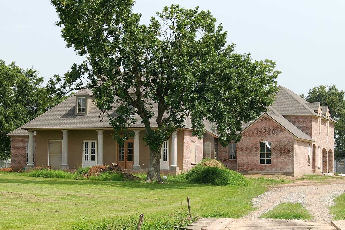 House plan exterior with brick and stucco, covered porch with columns, dormer window, and arched openings.