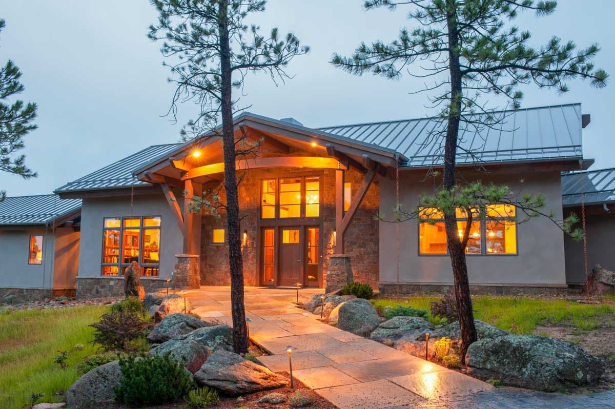 House plan exterior: Contemporary style, single-story with metal roof, stone accents, large windows, and covered entryway with exposed beams.