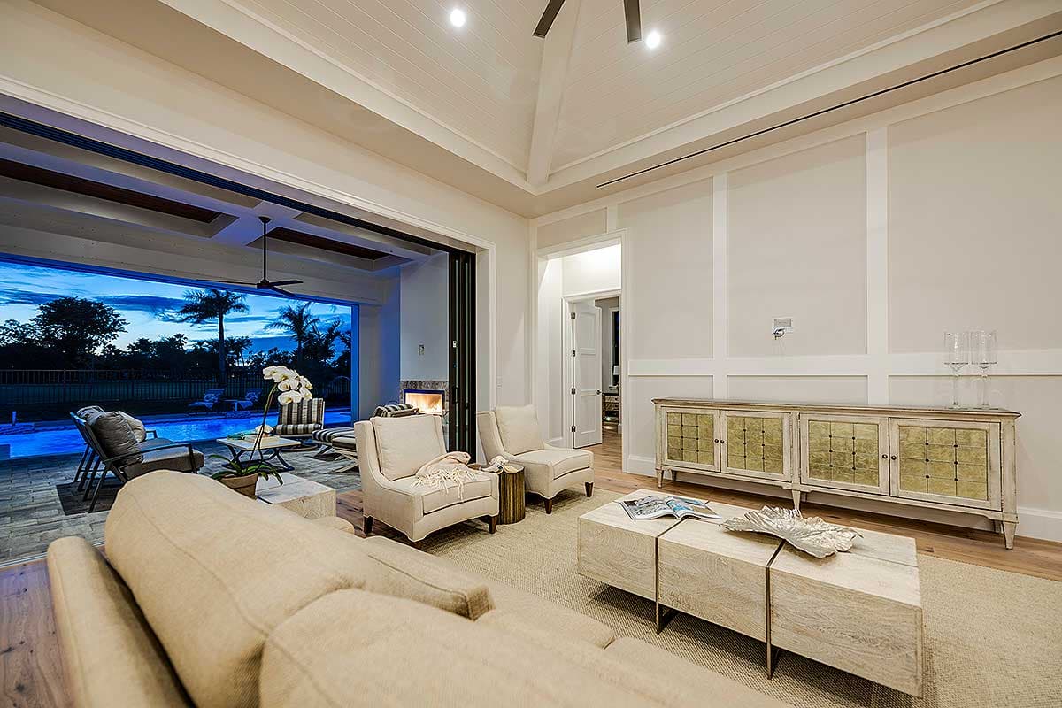 Living room with vaulted ceiling, fireplace, and large sliding doors opening to a pool area with palm trees.