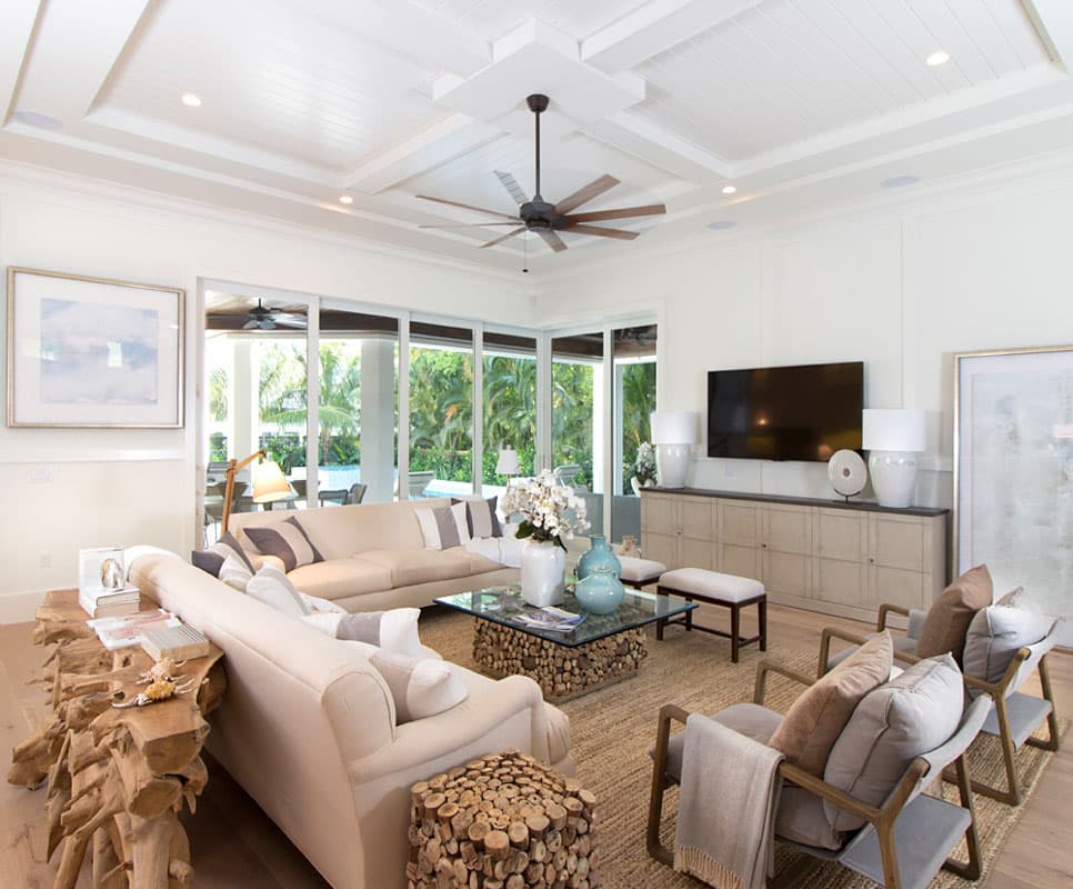 Living room with coffered ceiling, large sectional sofa, glass coffee table, and media console with television.