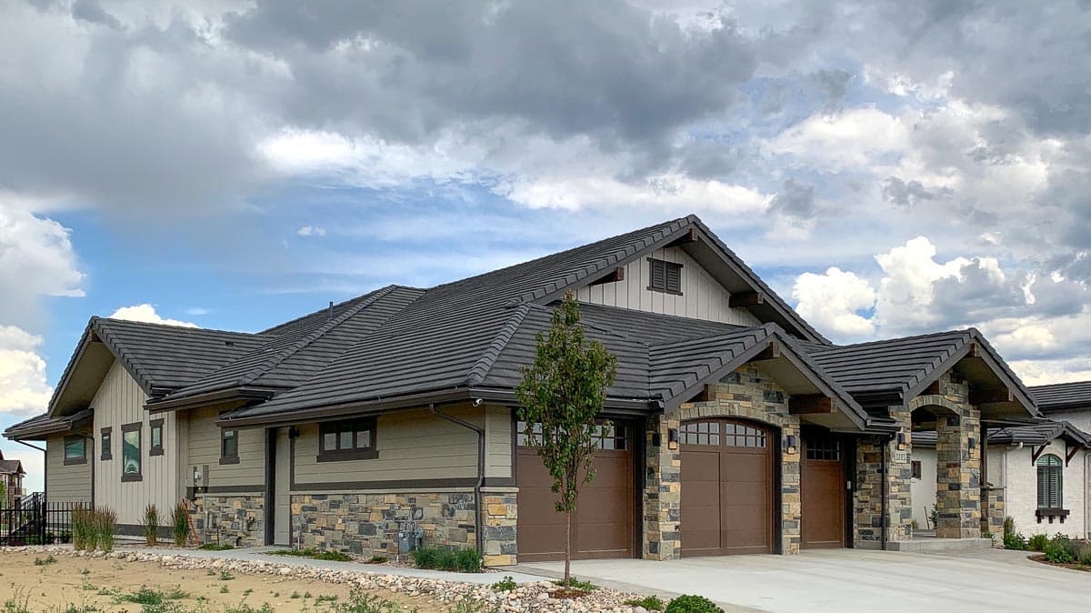 House plan exterior with stone accents, multiple gables, dark tile roof, and three-car garage with arched doors.