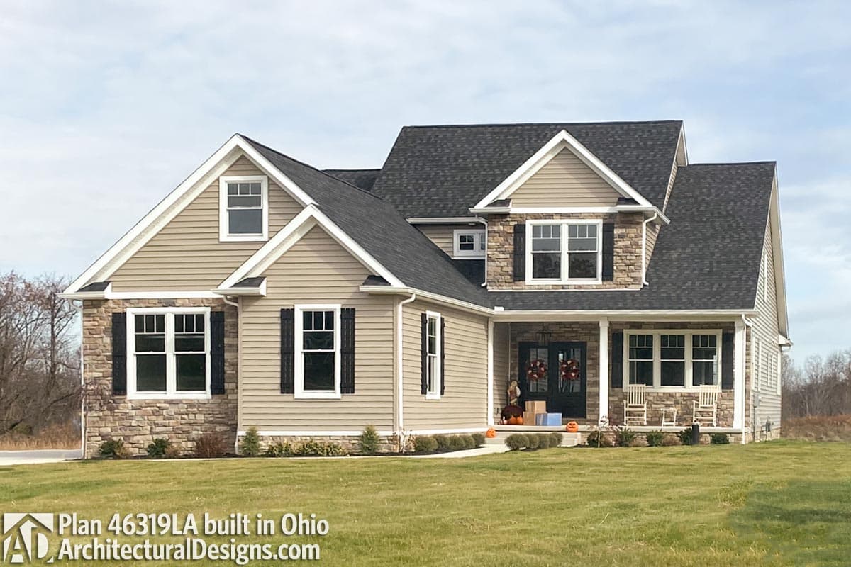 House plan exterior: Two-story home with stone accents, gables, dormers, and covered front porch with rocking chairs.