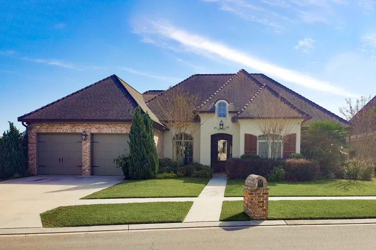 House plan exterior. Two-story with brick and stucco facade, arched windows, and a multi-gabled roof. Includes a two-car garage.