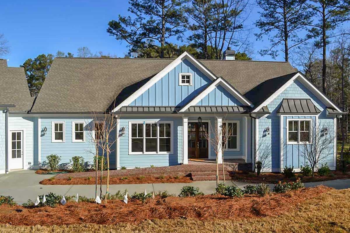 House plan exterior: Blue-sided one-story home with multiple gables, dormer window, and covered front porch.