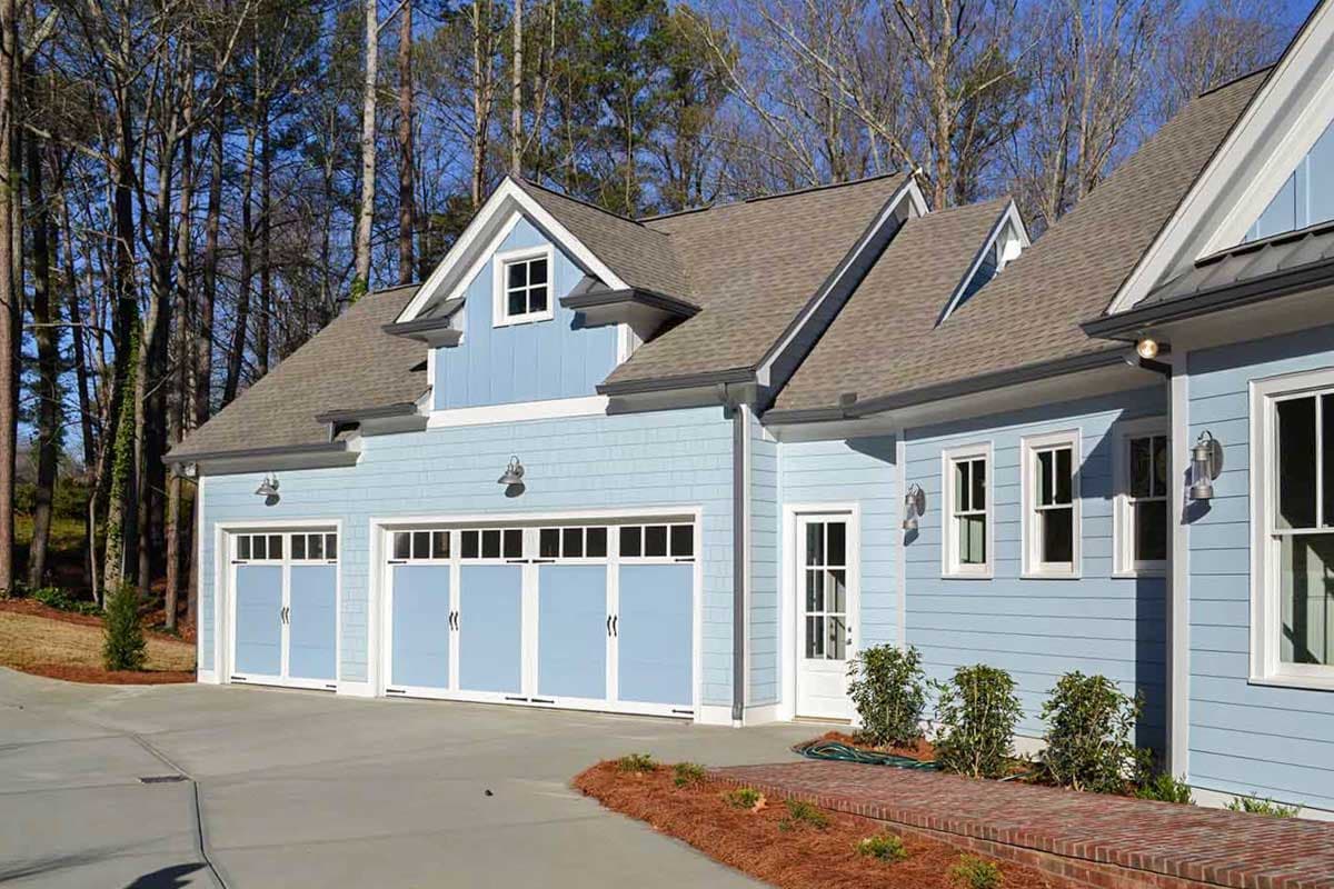 House plan exterior: Two-story modern farmhouse with three garage bays, a dormer, and shake siding.