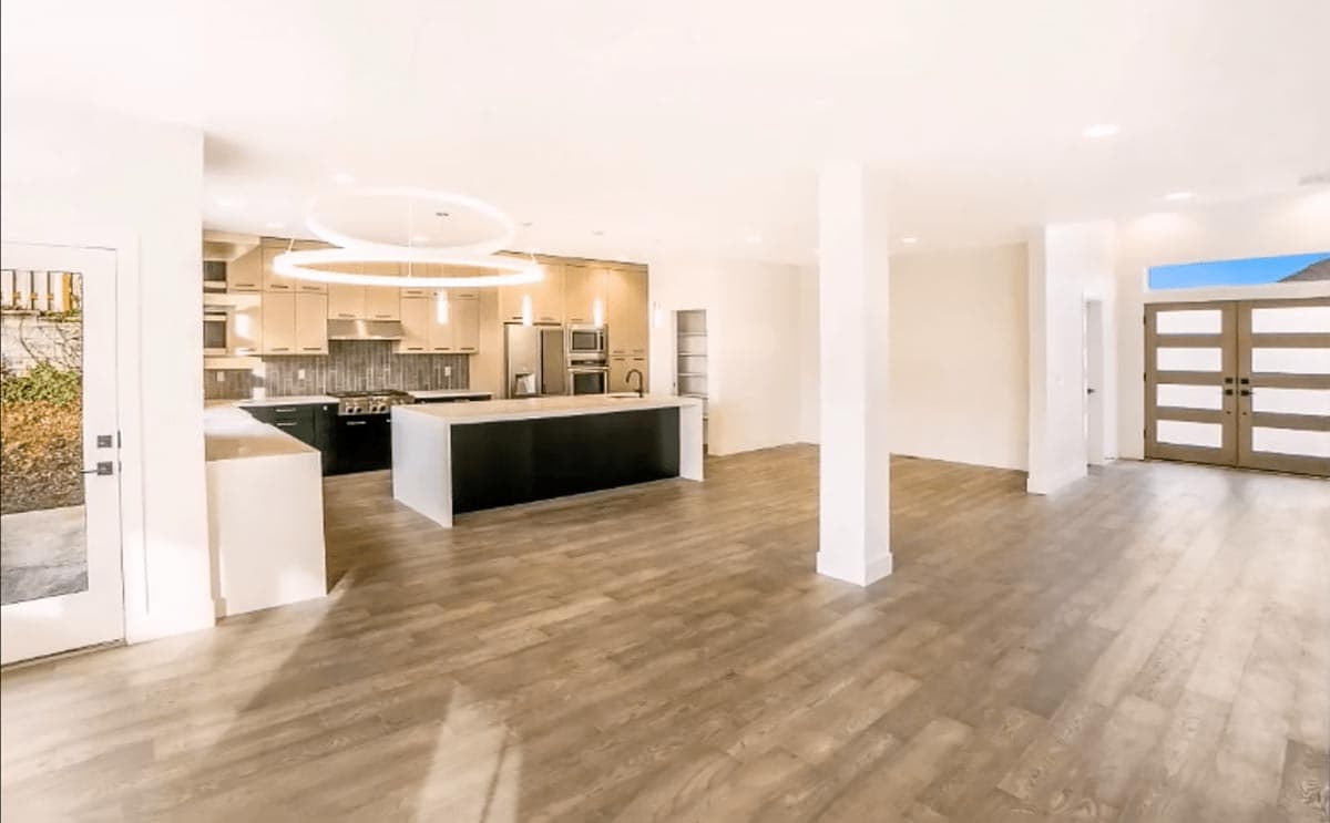 Open concept interior view of a modern kitchen with island, and double doors leading to the exterior.