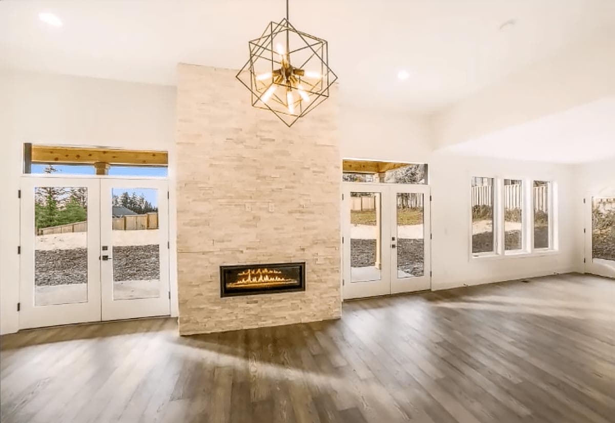 Open living area with stacked stone fireplace, modern chandelier, and double glass doors leading outdoors.