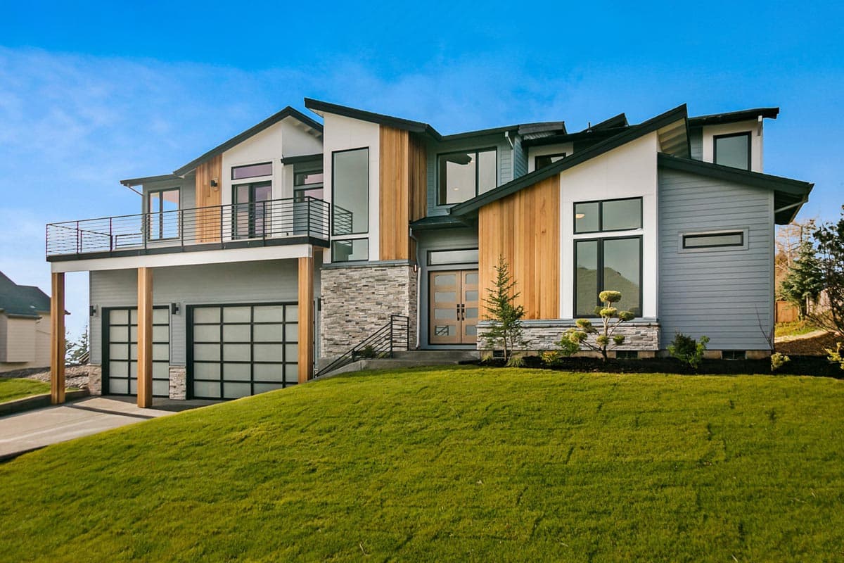 House plan exterior with modern design. Features include multiple gables, a second-story balcony, and a two-car garage with glass doors.