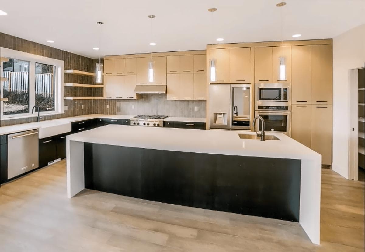 Modern kitchen with large island, light wood cabinets, stainless steel appliances, gas range, and farmhouse sink.