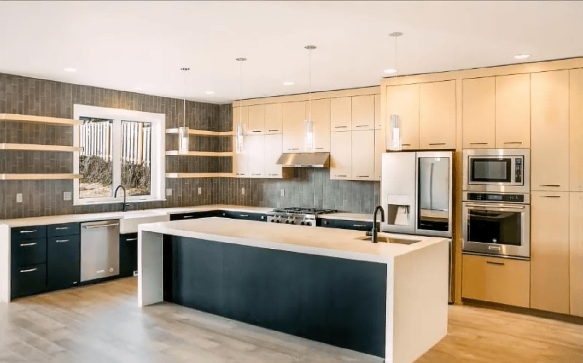 Modern kitchen with L-shaped island, light wood cabinets, dark lower cabinets, stainless steel appliances, and open shelving.